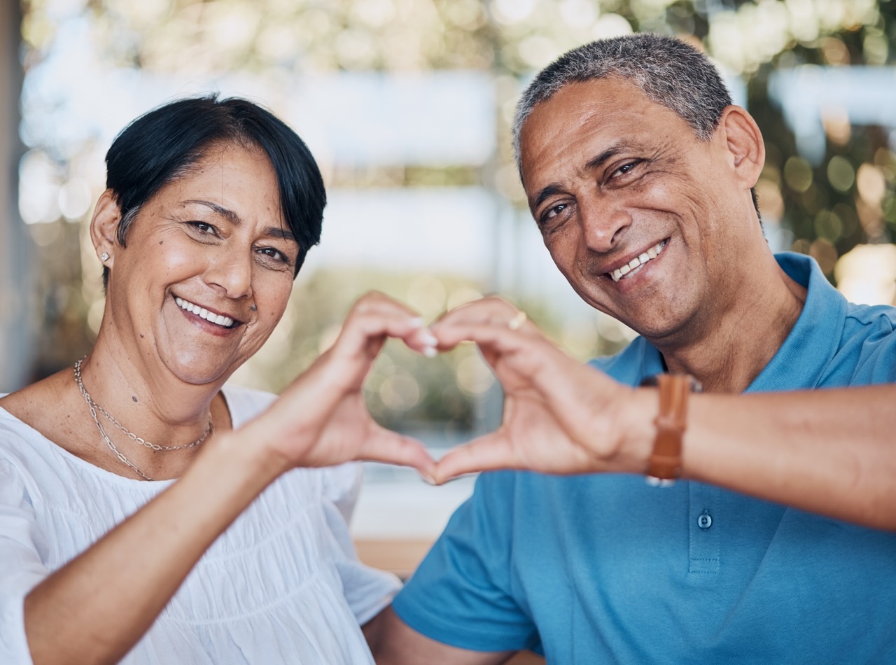 An older couple smiling together, making a heart shape with their hands